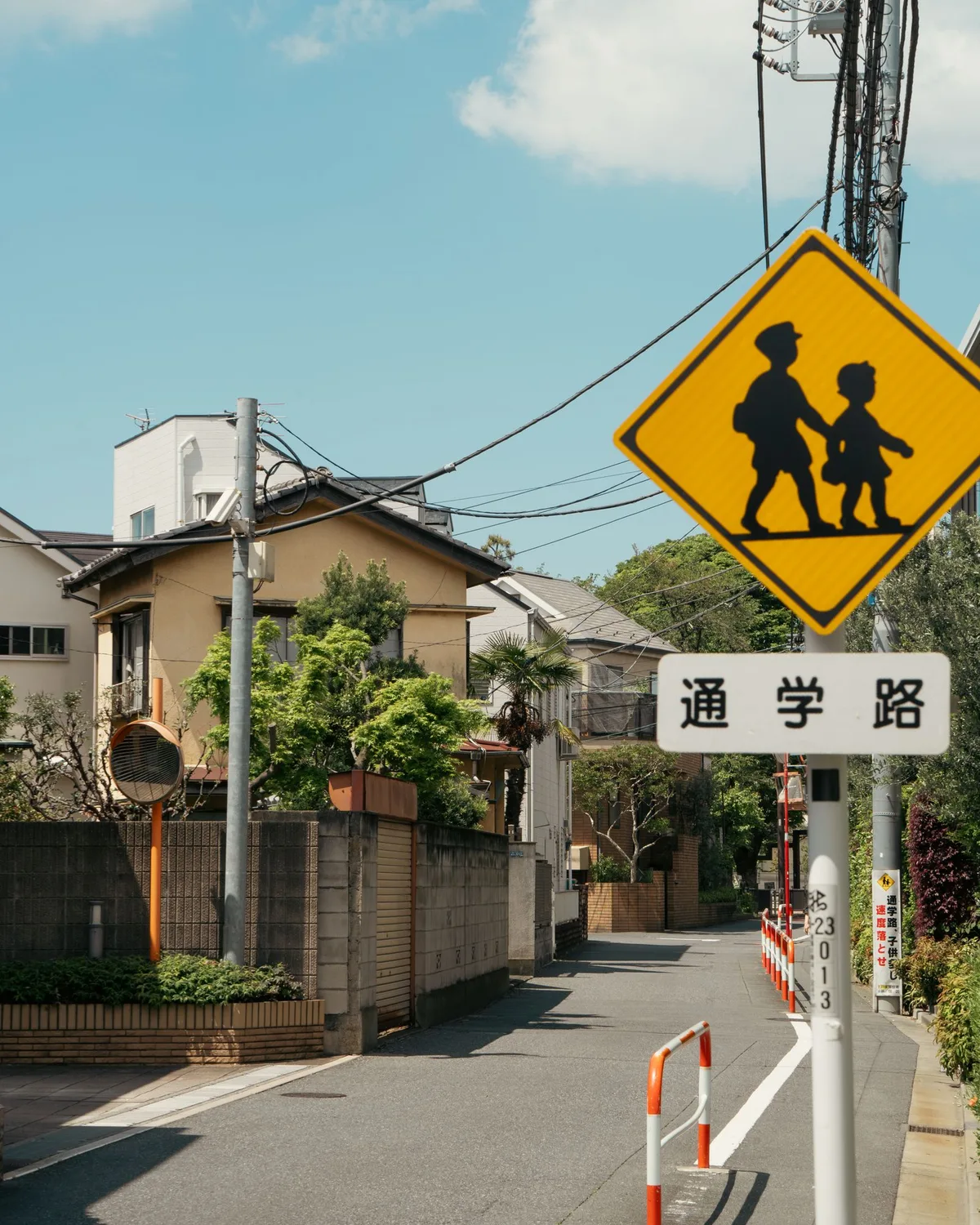 住宅街の細い道路に立つ「通学路」の標識と黄色い横断標識